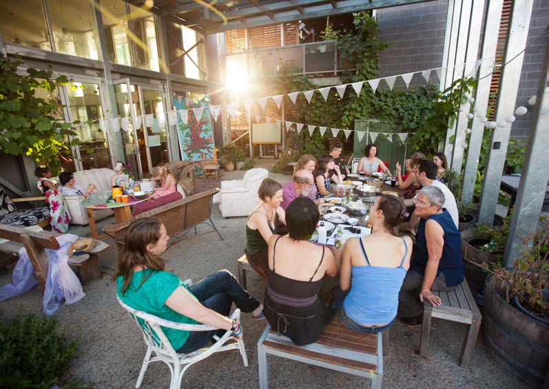 Photo: people sit around a table on a verandah underneath hanging flag pennants